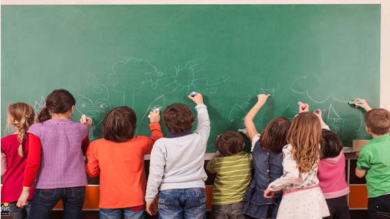 Group of nine children drawing on school chalkboard with chalks.