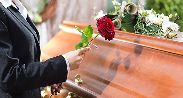Mourning woman on funeral with red rose standing at casket or co
